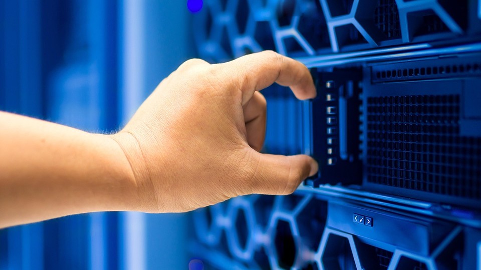 Close-up of a hand racking a server in a blue-lit data center